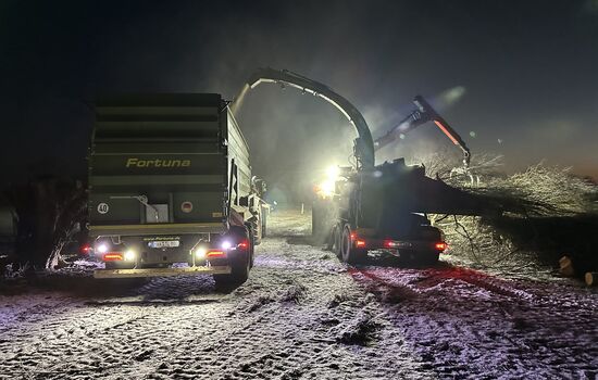 Traktor mit Hänger wird von einem Anbauhäcksler beladen