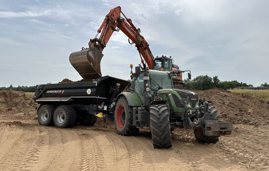 Trecker mit Anhänger wird von einem Bagger mit Erde beladen
