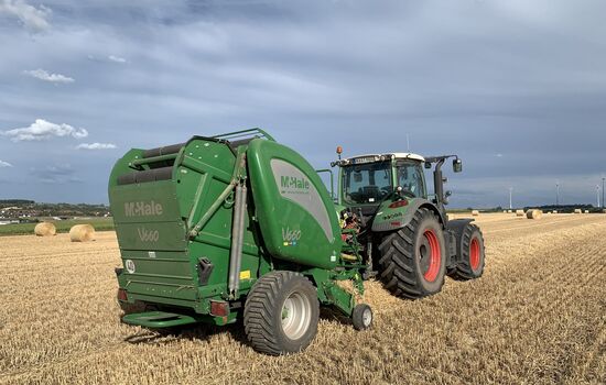 Seitenansicht einer Strohballen Presse bei der Arbeit auf dem Feld