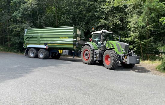 Trecker mit Anhänger steht auf einem Waldparkplatz
