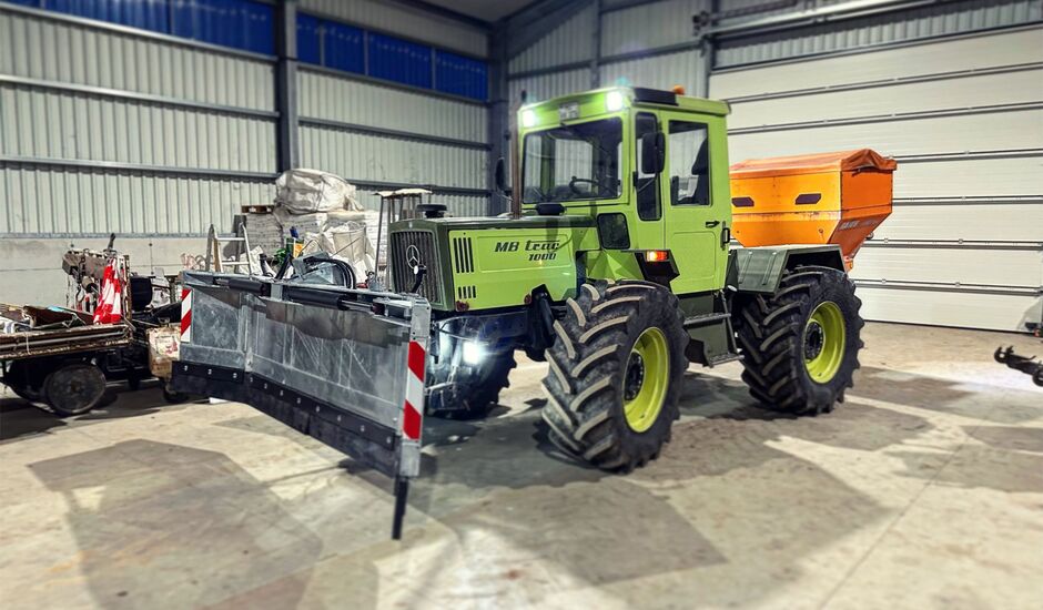 Linneshof GbR - Winterdienst Ein in einer Halle stehender Traktor mit angebautem Salzstreuer und einem Schneepflug