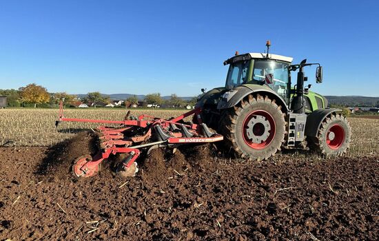 Seitenansicht eines Traktors mit heckanbau Pflug und Disk Walze bei der Arbeit auf dem feld